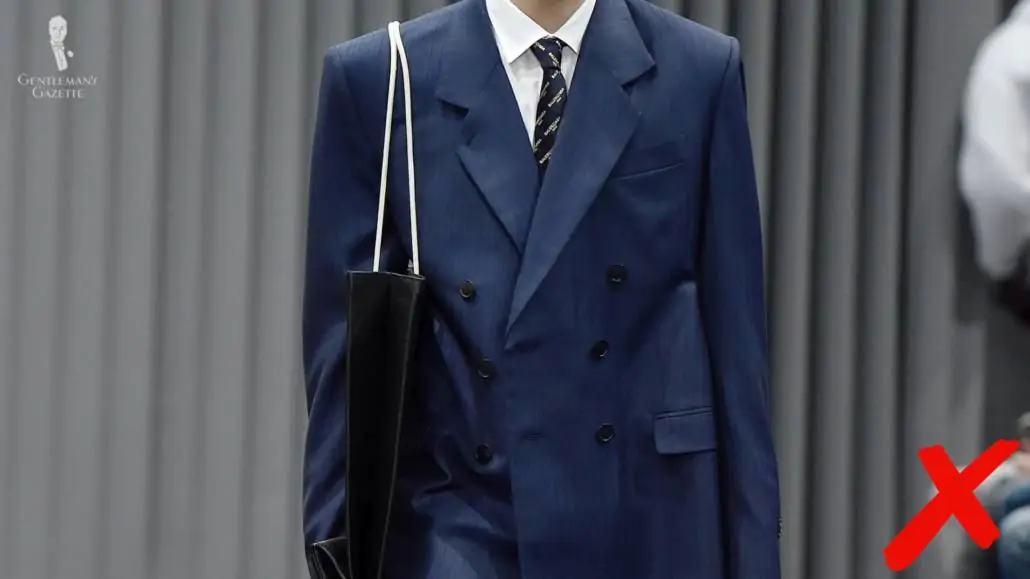 A model walking on a ramp with an oversized suit jacket. 