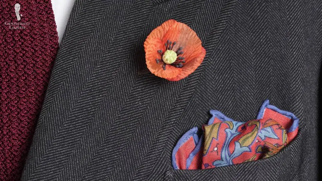 Orange poppy boutonniere on a grey jacket with matching accessories.