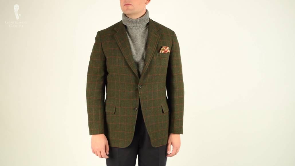 Raphael wearing an olive tweed jacket with check pattern, gray turtleneck, pocket square with a touch of yellow, and navy trouser.