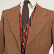 A tan herringbone jacket paired with a brown grenadine tie, white shirt, and striped vest with gold buttons