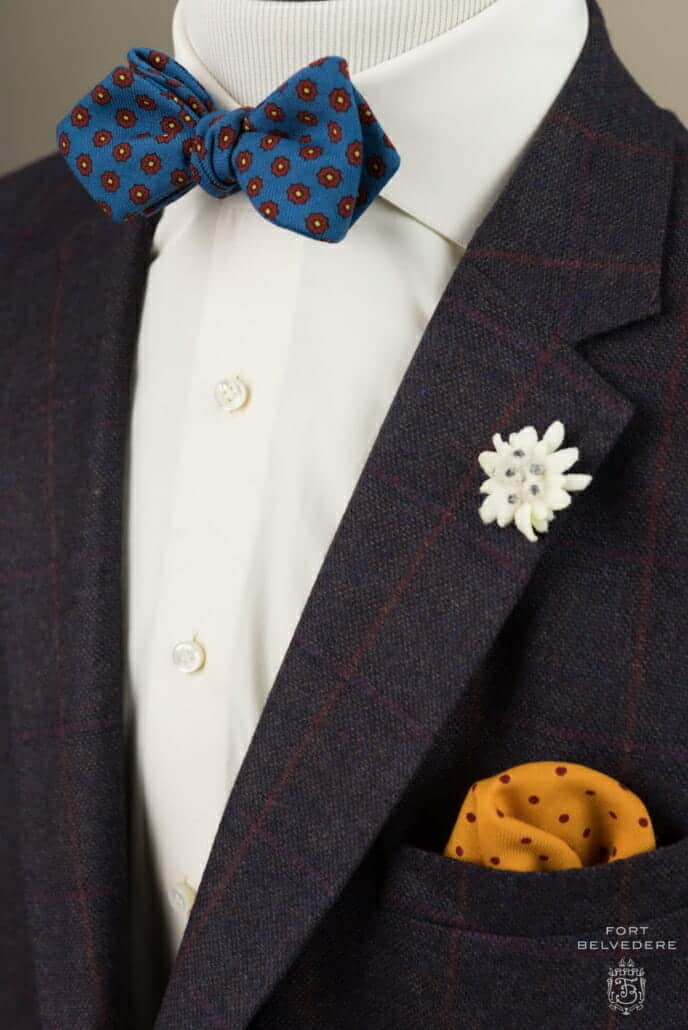 A wool jacket and a plain white shirt combined with an edelweiss boutonniere, a yellow polka dot pocket square and Bow Tie in Mohair Blue