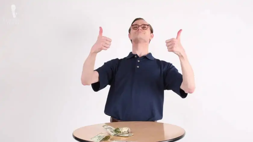 Preston with two thumbs up and money scattered on top of the table.