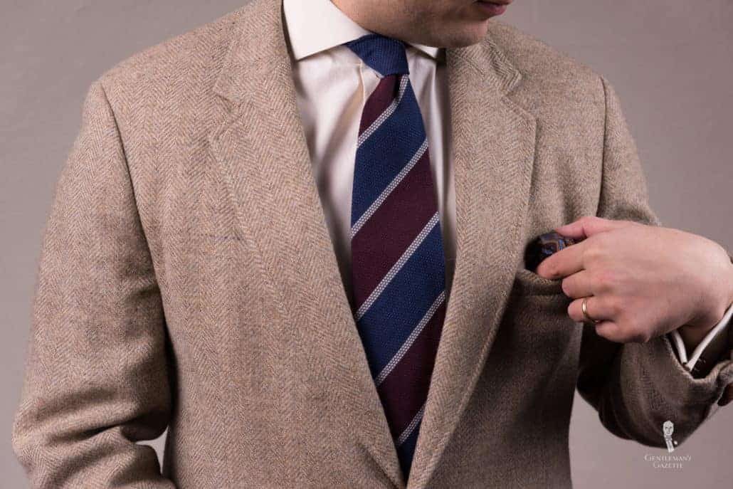 brown herringbone jacket paired with a red and blue grenadine striped tie.