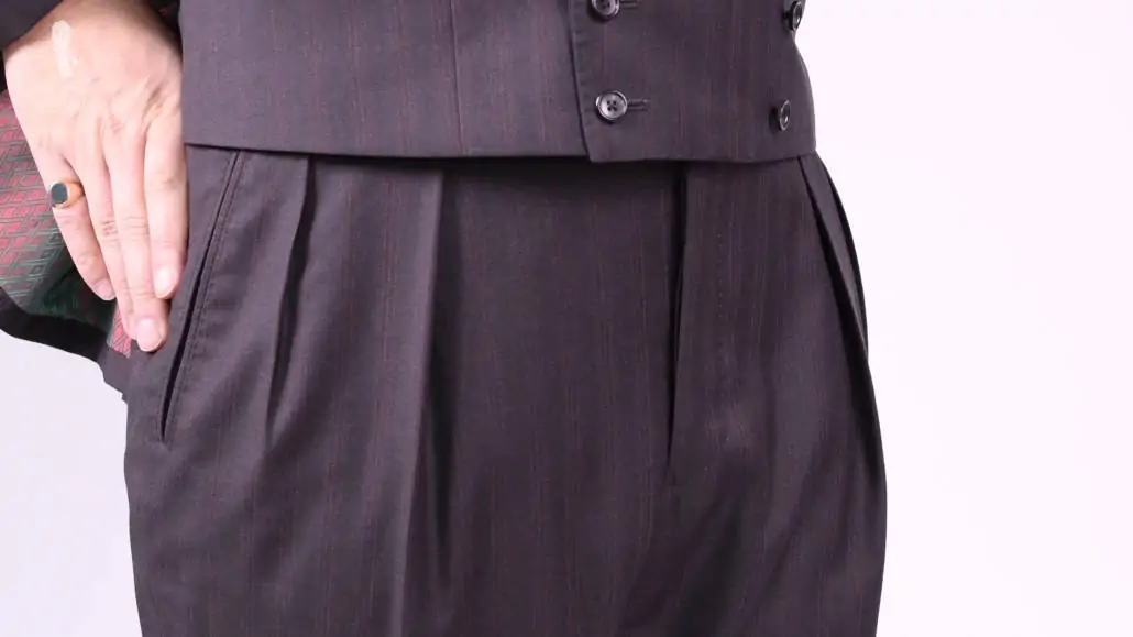 A pair of pleated trousers, worn as part of a three-piece suit.