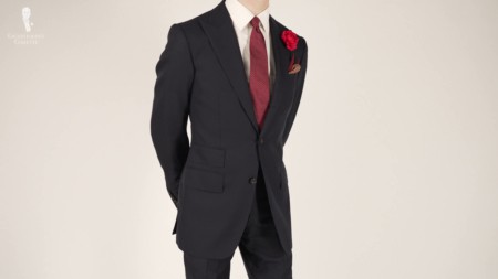 A man in a dark navy suit with red detailing like a red tie, boutonniere, and pocket square.