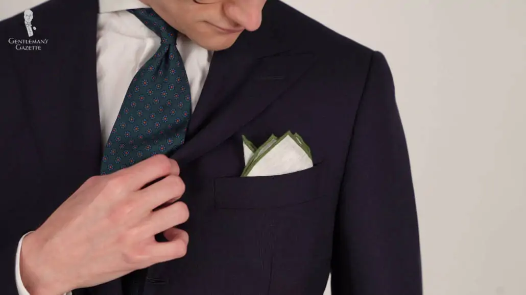 Preston wearing a navy suit with a white linen pocket square with contrasting green edge in a point fold.