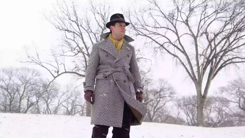 Raphael walking in the snow wearing a thick overcoat.