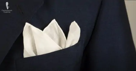 A plain white linen pocket square in a suit jacket pocket 