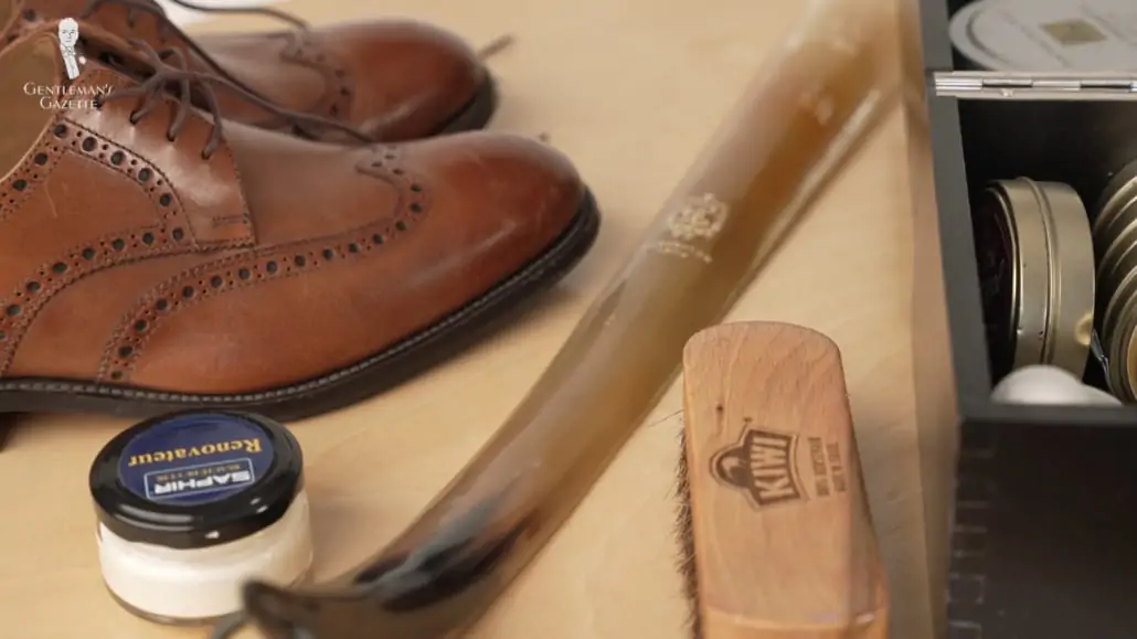 Brown brogue oxford shoes paired with mid brown shoe laces, a shoe polish and brush, and a shoehorn.