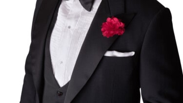The chest of a man wearing black tie with the shirt front, carnation, and pocket square visible