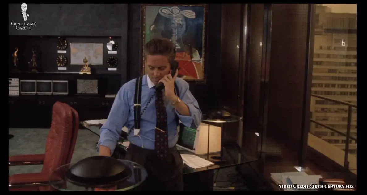 Gordon Gekko defying standard workplace fashion at the time: suit jacket not worn and donning a pair of charcoal pleated trousers