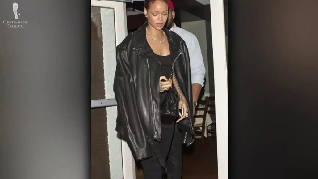 Rihanna walking out a restaurant with a black perfecto jacket draped over her shoulder
