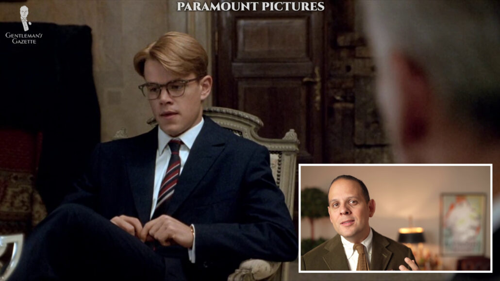 Tom Ripley wearing a navy suit with a striped tie.