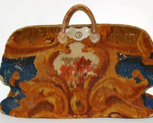 A simple piece of luggage made from oriental rugs and carpets, with an iron hinge at the top as the only structural frame to the bag.