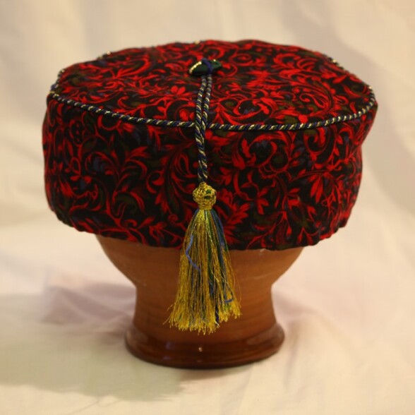 A red smoking cap with a tassel on a stand