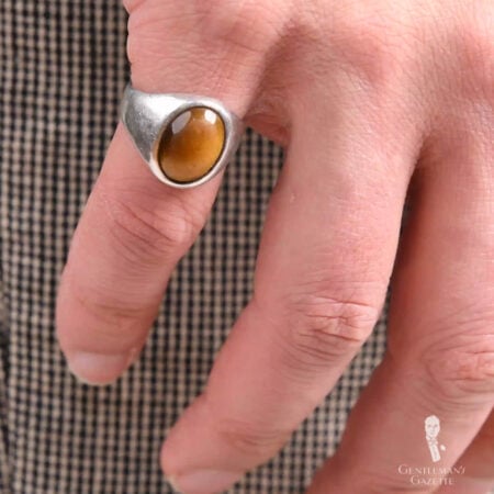 A photograph of a silver ring with an amber stone worn on the pinky finger