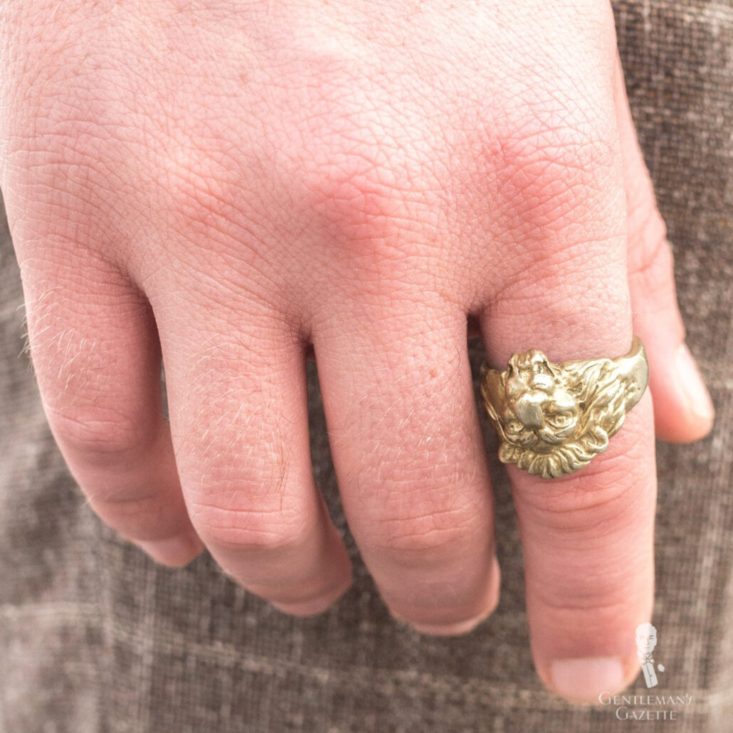 A photograph of a hand with a gold lion-headed ring on the index finger