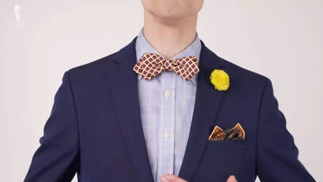 Preston wearing a dark navy suit with a printed bow tie, a pocket square with a tinge of gold and a yellow dandelion boutonniere.