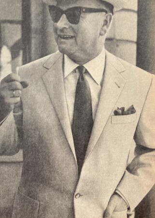 A black and white photograph of a man in a suit wearing his wedding ring on the ring finger of his ring hand