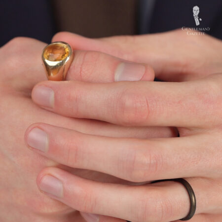 A photograph of a hand with a gold ring with an orange stone on the thumb 