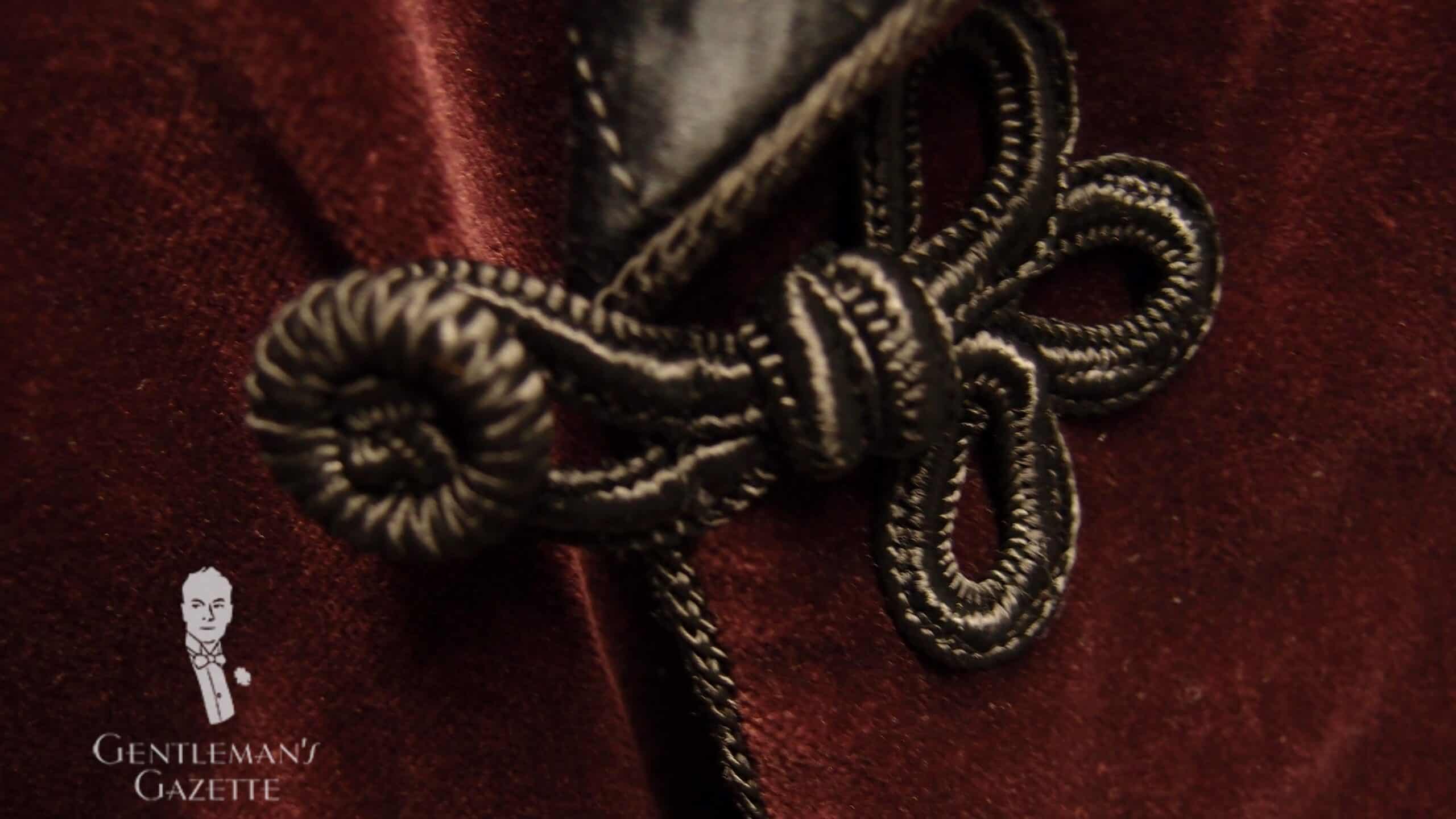 Burgundy Smoking Jacket With Black Frogging And Toggles Scaled A photograph of the toggle and frogs on a smoking jacket