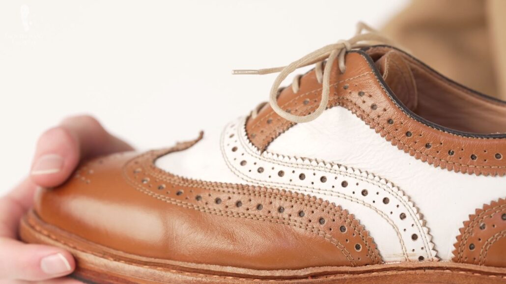 A close up of the broguing in a brown and white spectator shoe