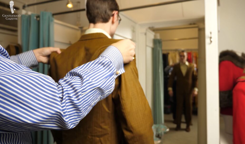 Raphael assists Preston in fitting a jacket in front of a mirror