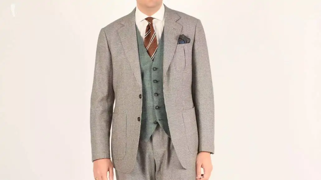 Dark green silk pocket square paired with a bluish-green tweed vest, a houndstooth flannel suit in dark brown and off-white as well as a white shirt, and a brown and green striped shantung silk tie.