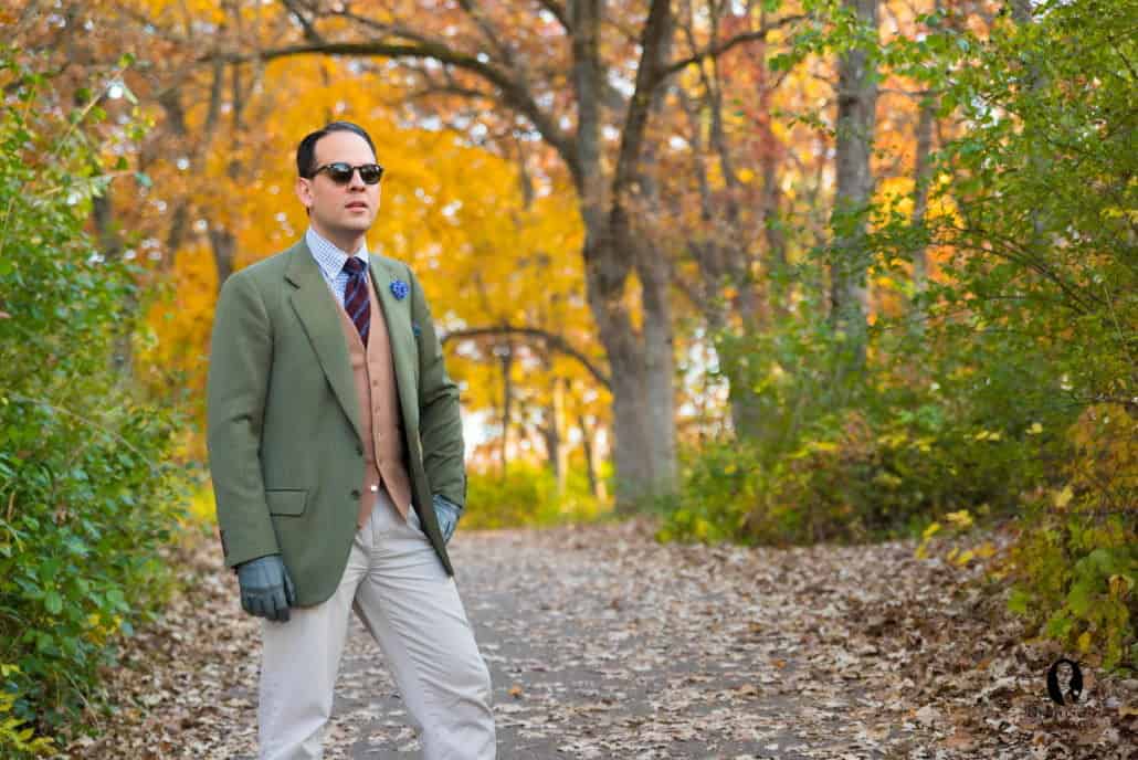 Raphael wearing an olive green coat with a tan vest, diagonal stripe tie, white & blue check shirt, Blue Cornflower Boutonniere, & cream pants plus green gloves.