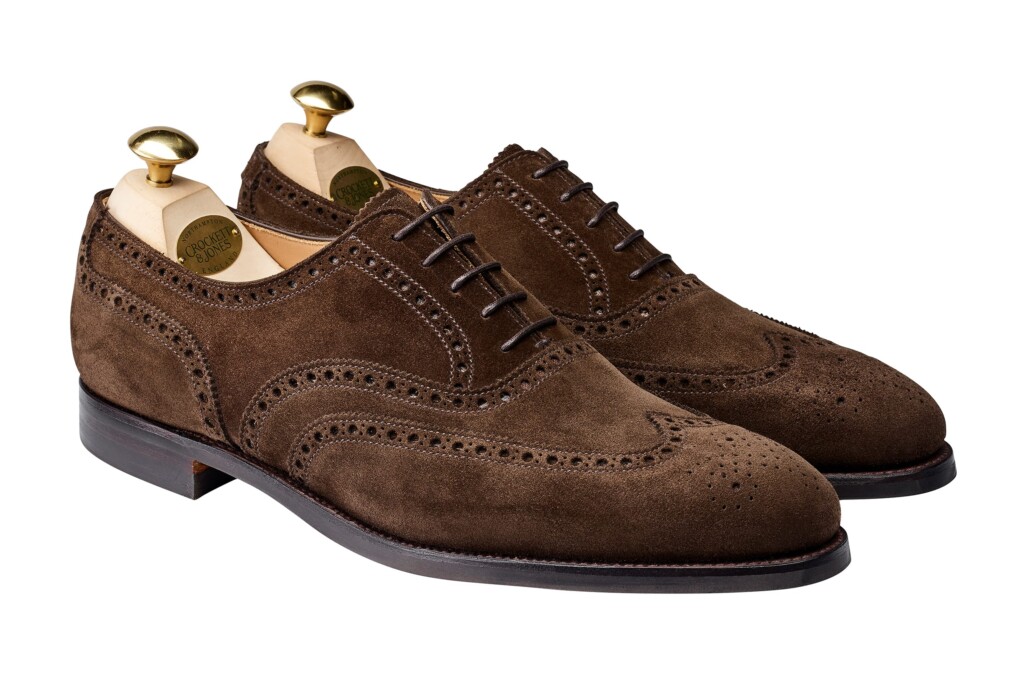 Crockett and Jones produces classic Oxford styles such as this dark brown model in suede featuring a wingtip with broguing