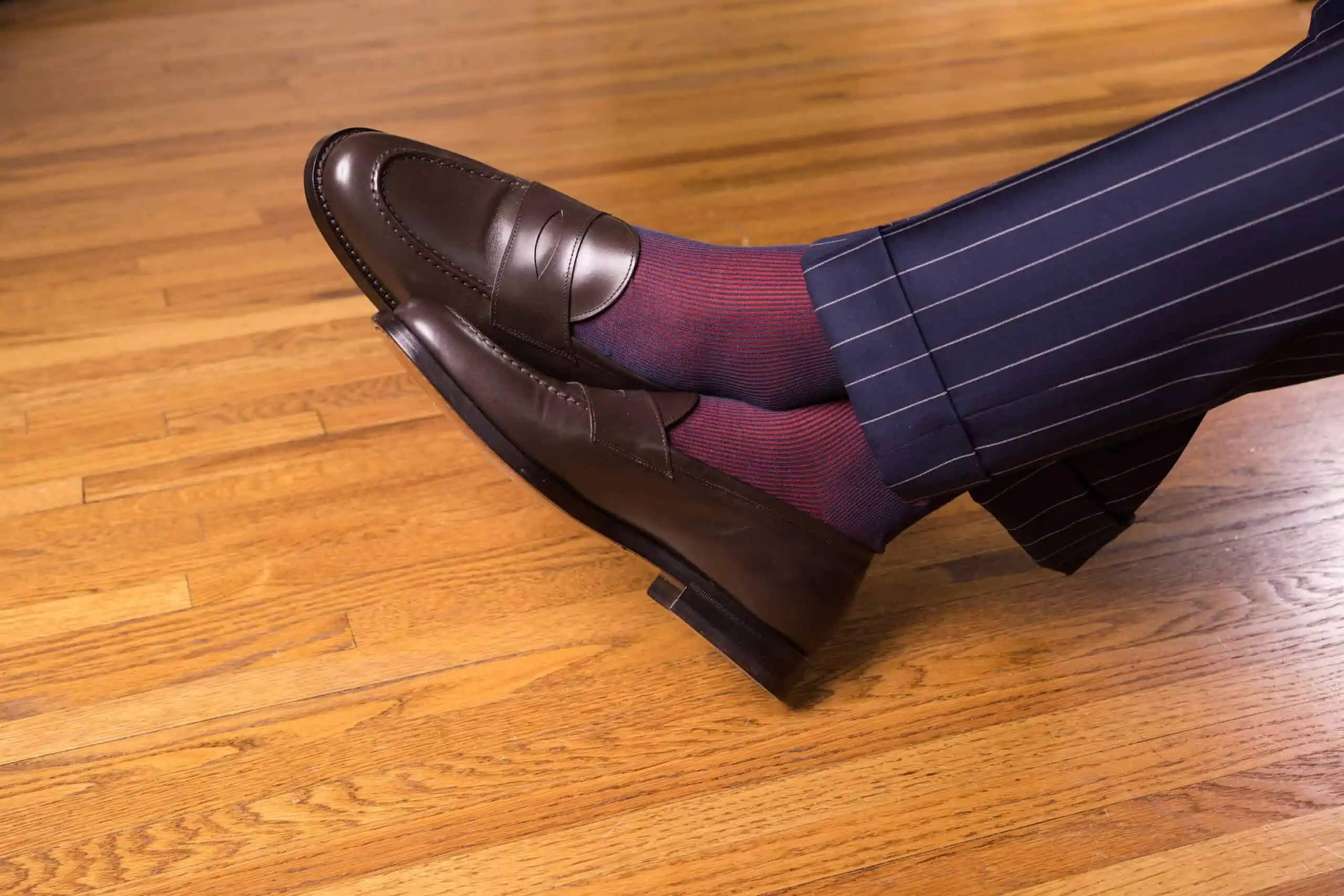 A photo of Dark brown penny loafers with red and navy socks and navy pinstripe pants