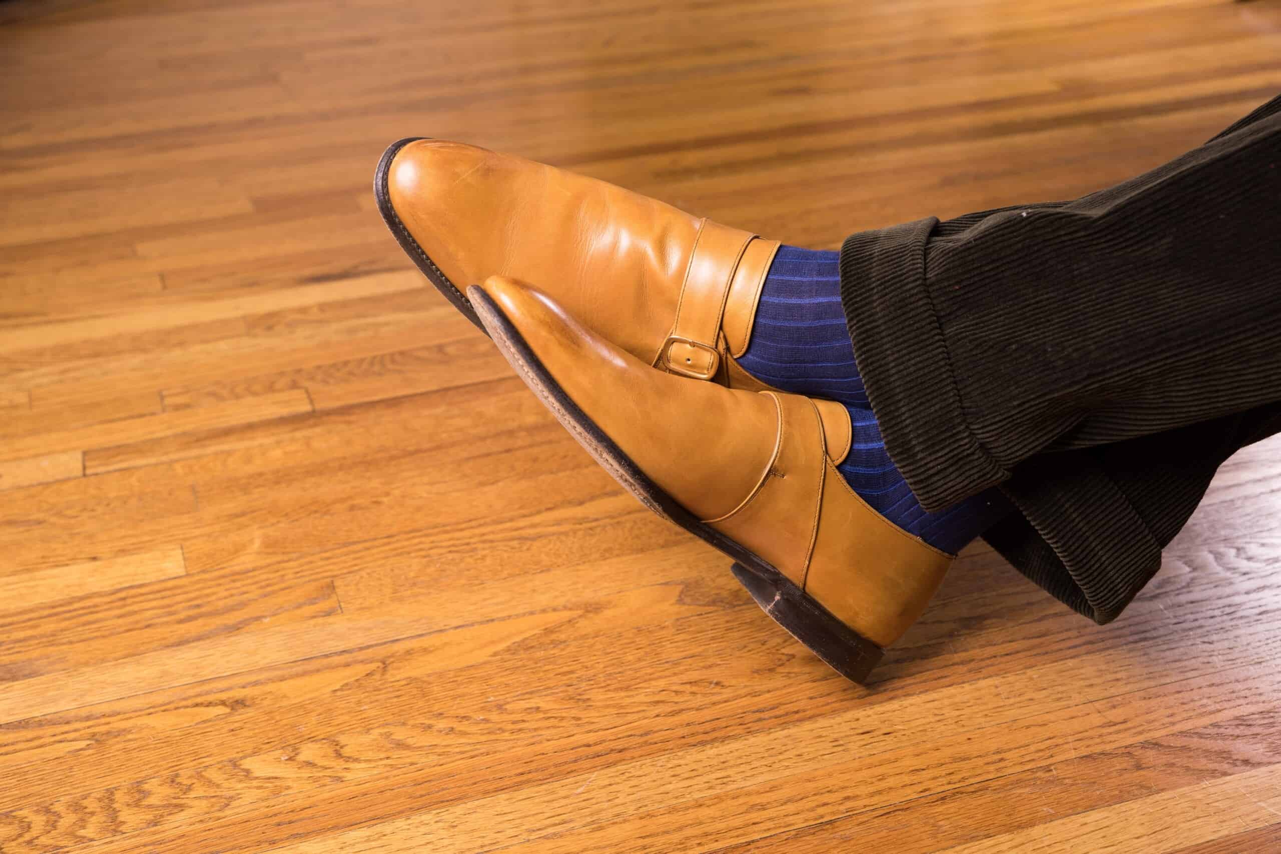 Light tan single monkstrap shoes with blue socks and dark olive corduroy trousers