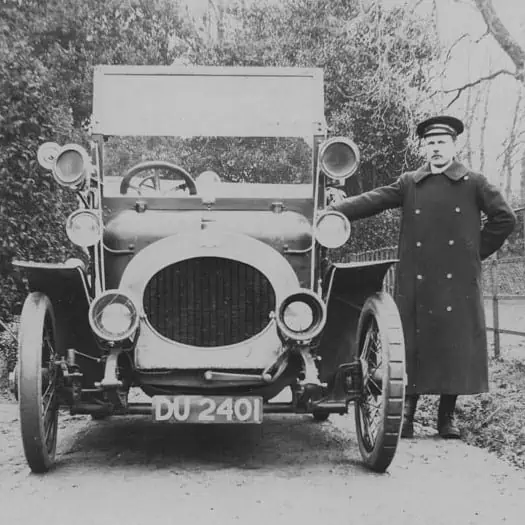 A photograph of a chauffeur next to a primitive car