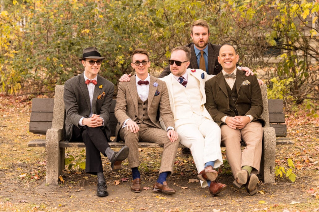 Four men seated at a bench with a fifth standing behind all wearing suits