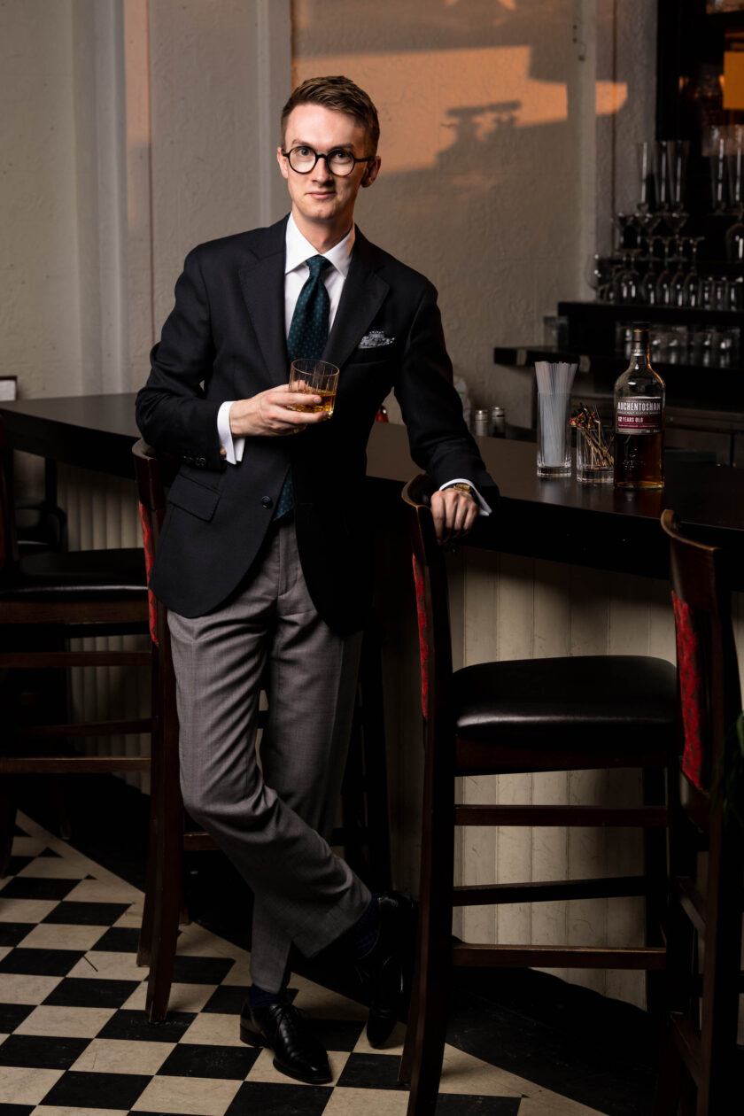 A man in a cocktail attire suit stands at a bar