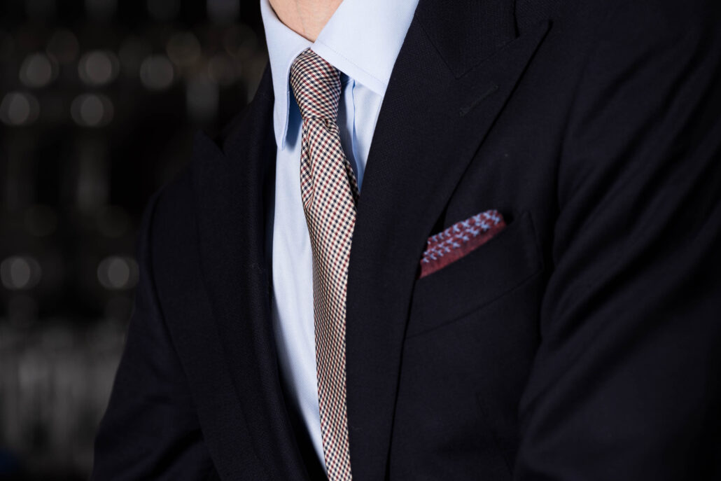The front of a dark navy suit with a blue shirt and red and blue accessories 
