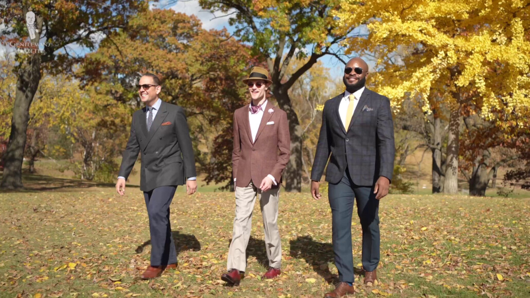 Three men in classic suits walk through a park as the leaves change 