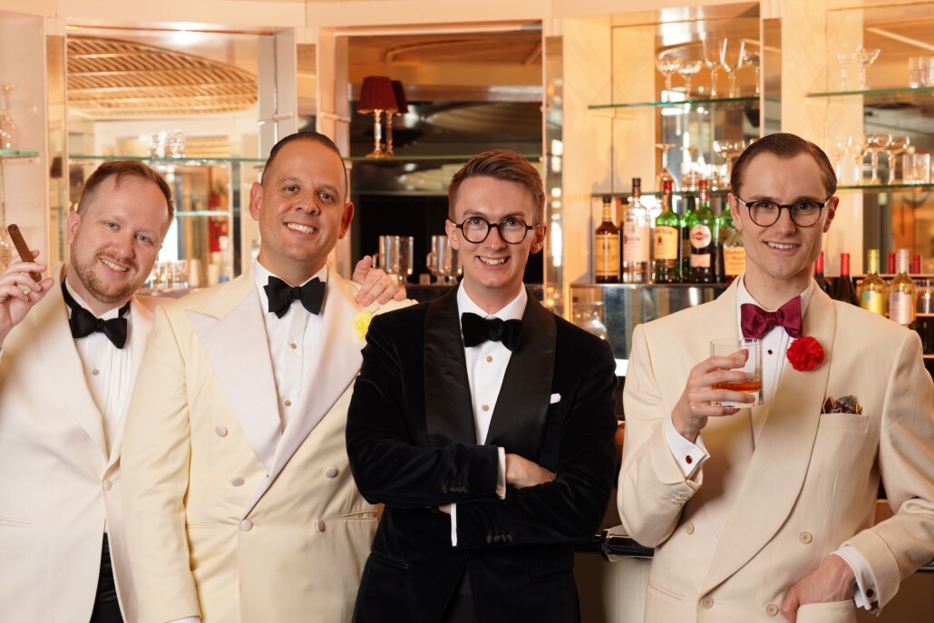Four men wear Black Tie ensembles in front of a bar