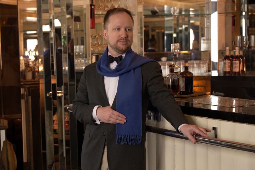 A man wearing a blue scarf at a bar with a sportcoat 