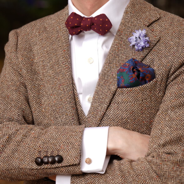 A photo of a tweed outfit in brown herringbone with bow tie, boutonniere, cufflinks and pocket square