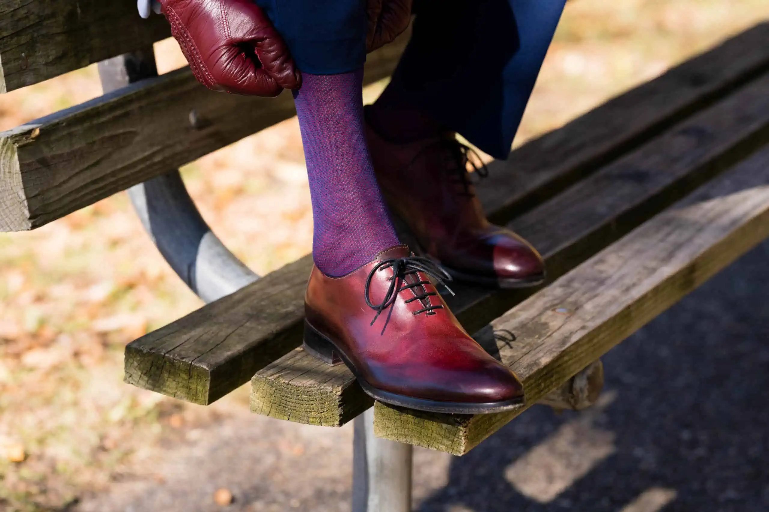 Oxblood shoes and blue and red socks on a bench in the fall