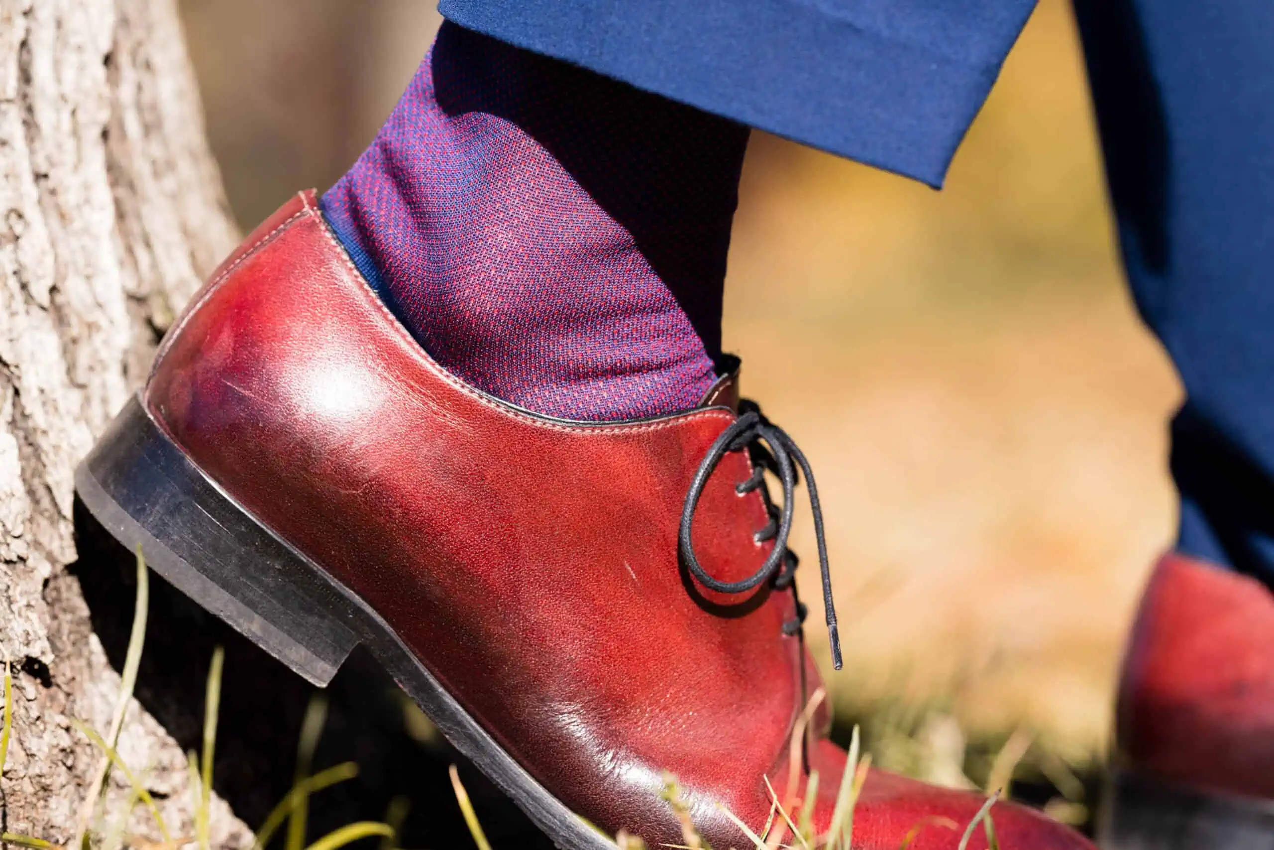 Close up of oxblood shoes with red and blue socks and a blue trouser cuff