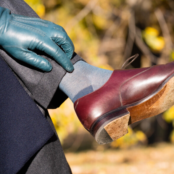 A photograph of a blue sock worn with oxblood shoes and a blue glove
