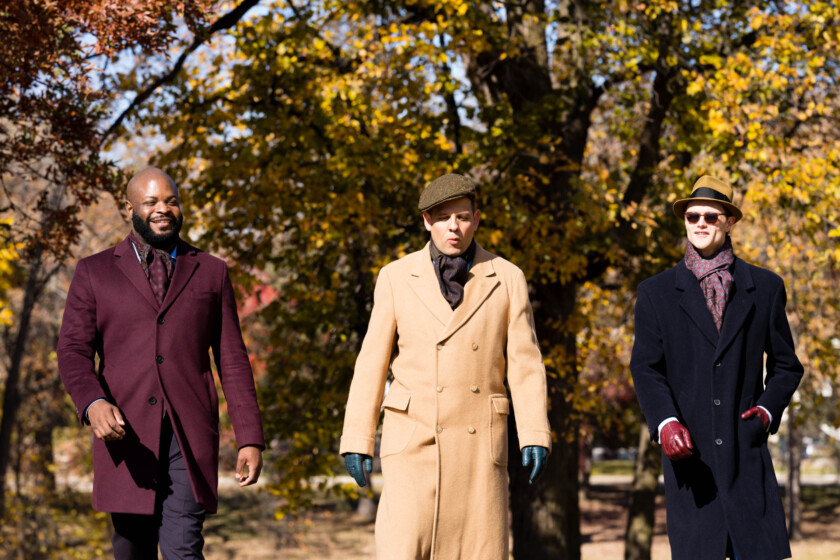 Three men in coats walk through a park during the fall