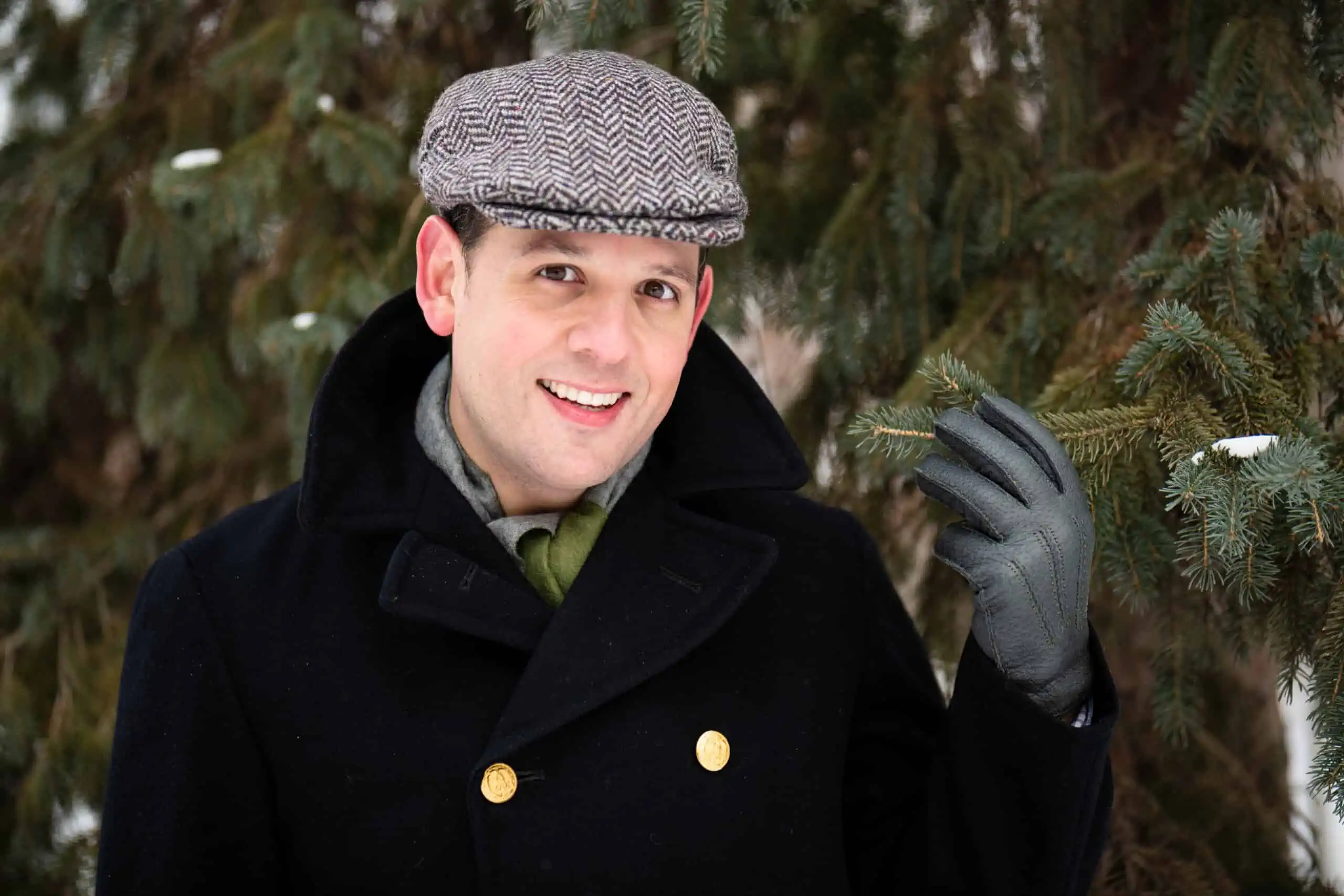 Raphael raises his hand while wearing a navy pea coat, flat cap, and grey gloves