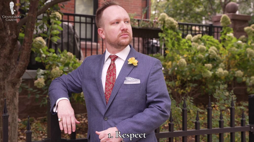 Sporting a navy suit jacket, red silk necktie, peach spray buttonaire, and a white pocket square.