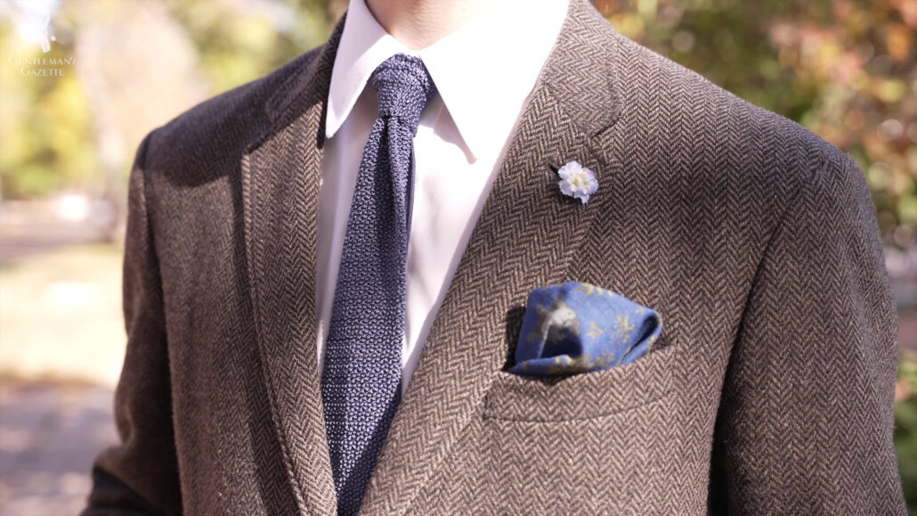 The pop of color of a navy blue knit tie in this suit ensemble. Knit Tie in Solid Navy Silk - Fort Belvedere, Light Blue Delphinium Boutonniere Buttonhole Flower Fort Belvedere