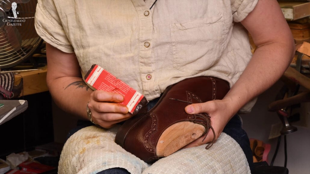 Amara using the Yankee wax to shine the heel of Raphael's shoe.