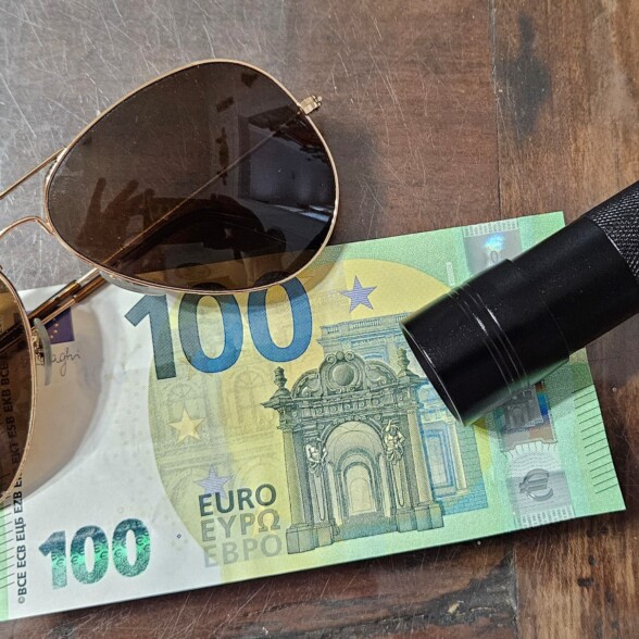 Photo of sunglasses, a UV flashlight, and 100 euro note
