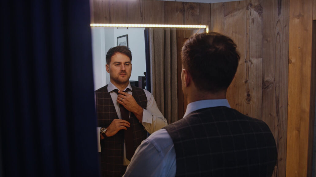 A man standing in front of the mirror tying his tie